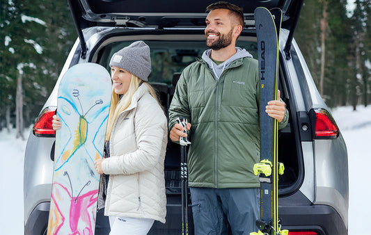 A couple outside in the snow holding a snowboard and skiis