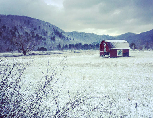 Red barn sitting in a snowy meadow located in Valle Crucis with mountains in the background. A quilt pattern - the carpenter's wheel - is on the side.