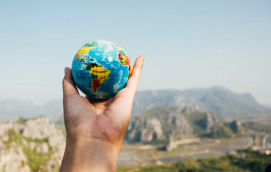 A hand holding a model of the earth in front of a scenic mountain landscape