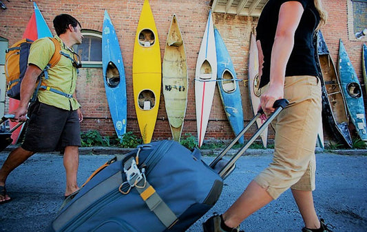 Travelers oulling luggage on a street in front of a row of kayaks