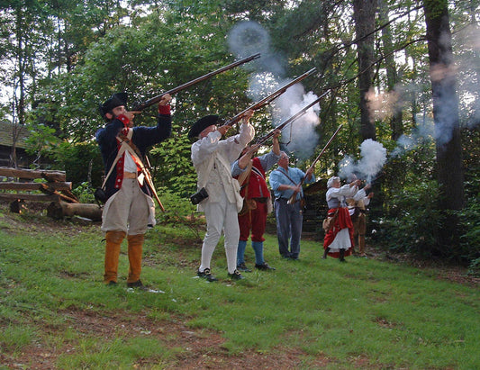 Colonial soldiers firing long rifles and pistols in a forest setting.