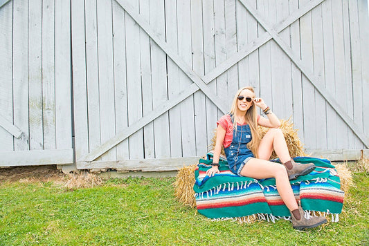 Woman wearing a overall shorts sitting on a hay bale