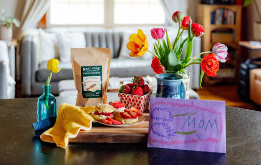 A tqablesetting with jam and biscuits and flowers in a vase and a mother's day card.