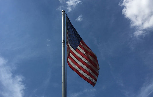 The flag of the United States on a flagpole with  a blue sky in the basckground.