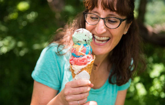 A smiling woman with a tripple scooped colorful icecream cone.