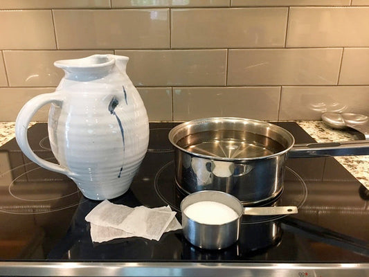 Pot on a stove with a tea pitcher, tea bags and a cup of sugar.