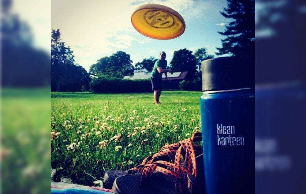 A man throwing a Frisbie in a field with a Kleen Kanteen bottle in the foreground