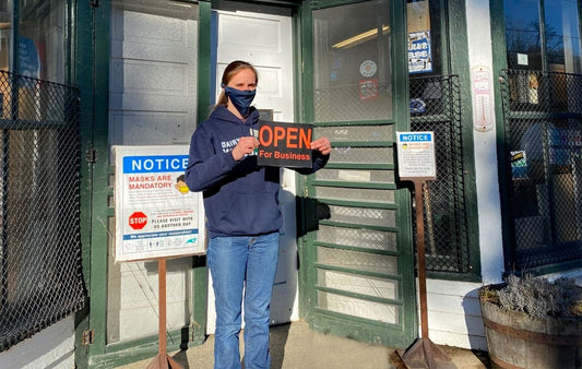 An employee wearing a mask amd holding an open sign outside the Original Mast Store