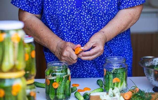 woman with may pickle jars on a table peeling carots to add to the pickles