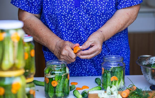 woman with may pickle jars on a table peeling carots to add to the pickles