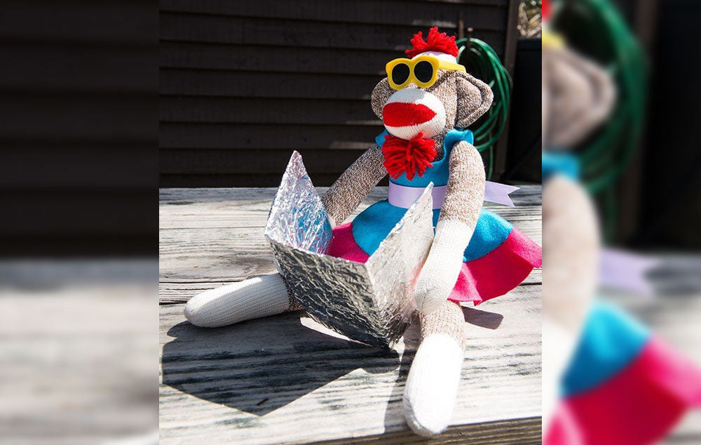 Sock monkey wearing sun glasses tanning itself on a deck