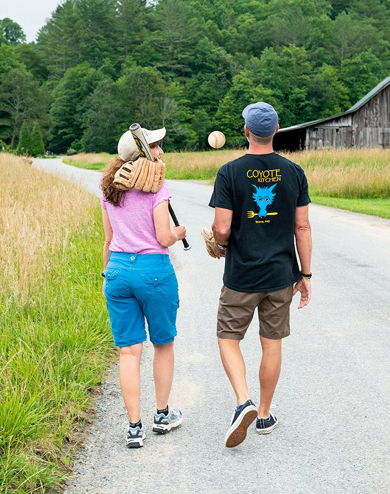 a male and female softball player walking on a country road.