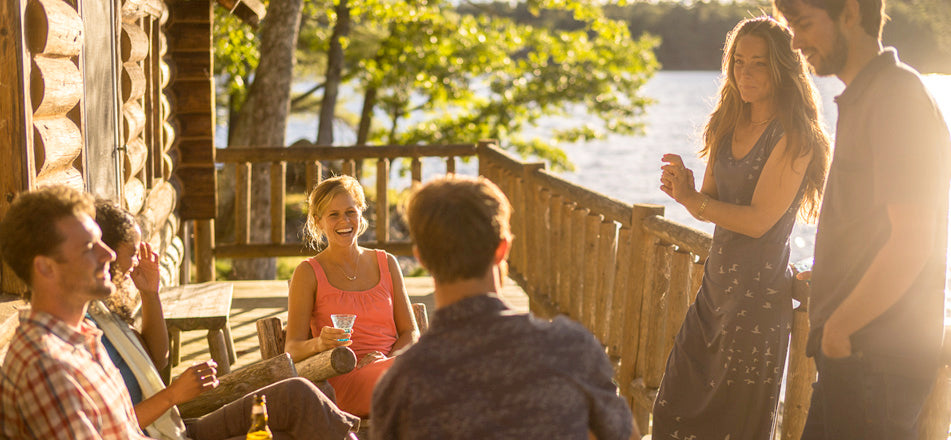 People having drinks and relaxing on a deck next to a lake wearing Toad&Co clothing