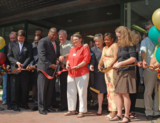 Group of people in front of a building doing the ceremonial ribbon cutting to open a business. Photo of Columbia location opening features dignitaries - Mayor Benjamin, John Cooper, opening general manager Ruth Smyrl, and to far right Lisa Cooper.