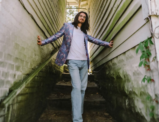 A man with long brown hair and glasses stands on a stairway between two white walls.