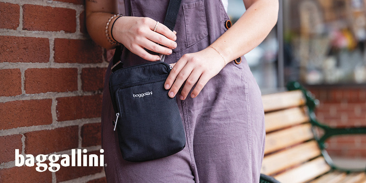 Person holding a black Baggallini purse against a brick wall.