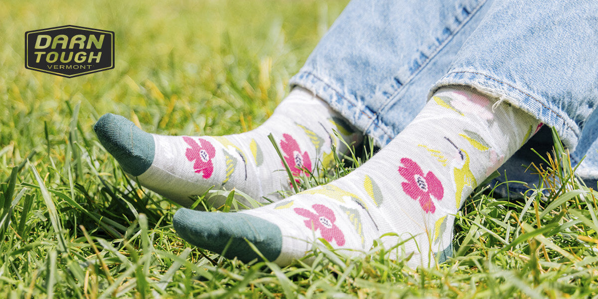 Person wearing a pair of floral Darn Tough socks and jeans on grass.
