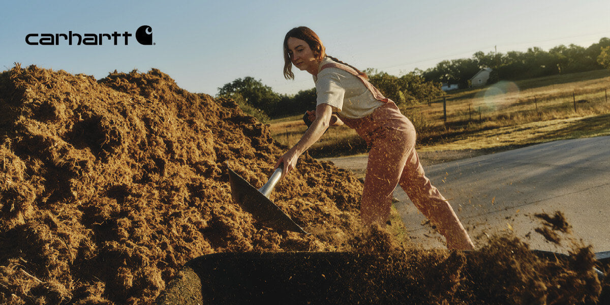 Women shoveling dirt wearing a Carhartt overalls.