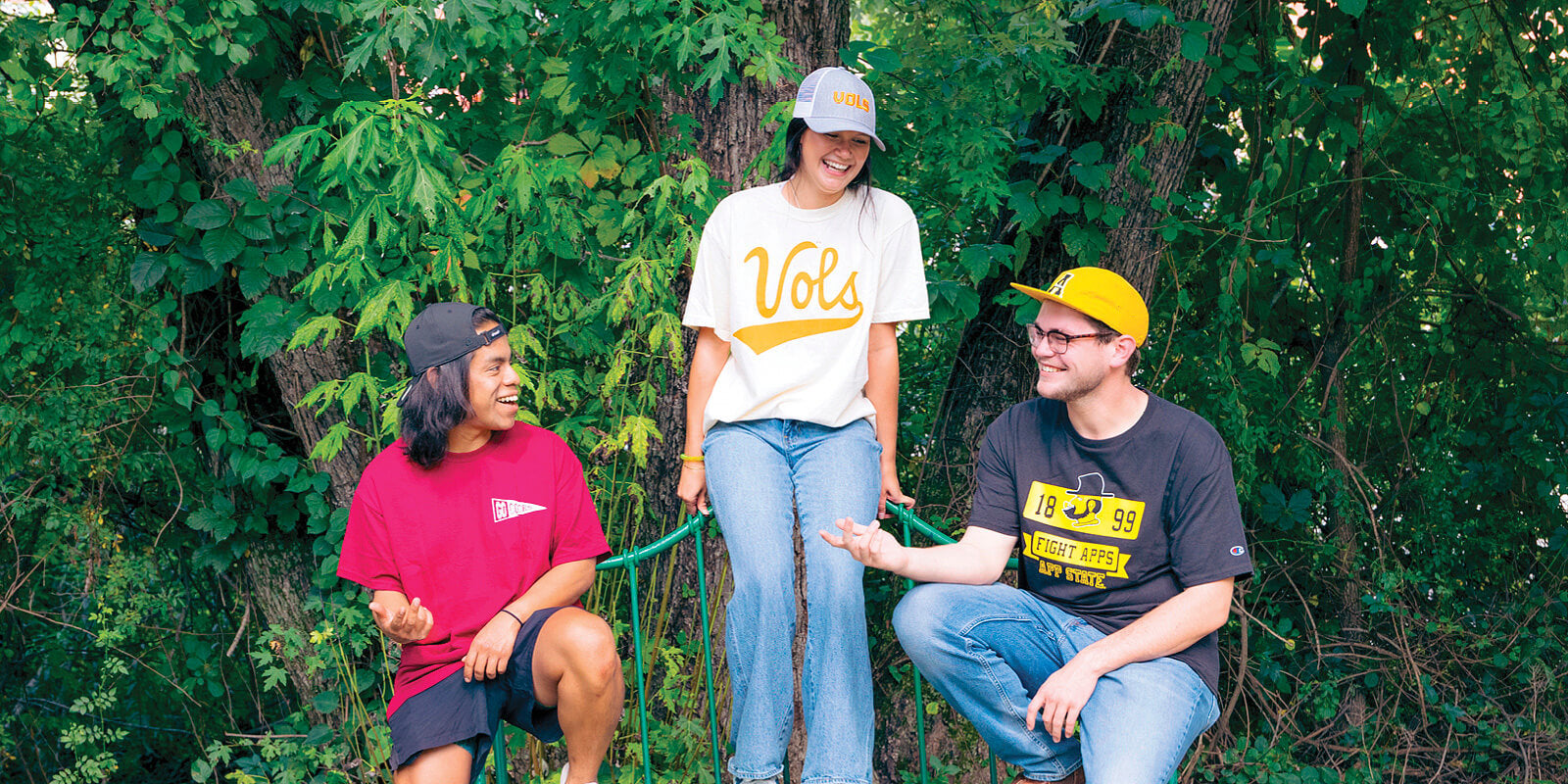 Three college students sitting on a park bench, wearing University of South Carolina, University of Tennessee, and Appalachian State University apparel