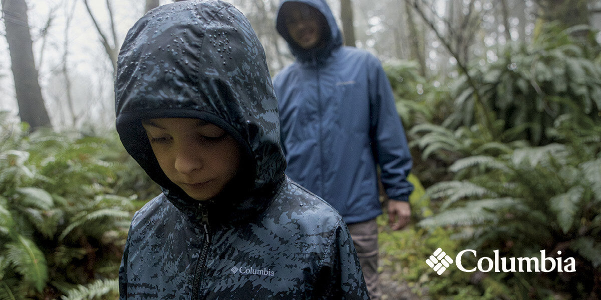 A child and a man wearing Columbia rain jackets walking through the rain in a forest.