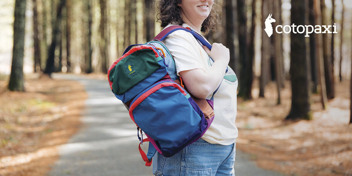 Woman with a colorful Cotopaxi backpack in a forest.