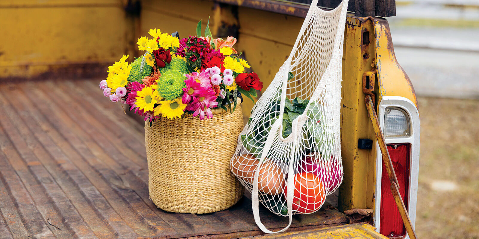 Wicker basket with colorful flowers and a market bag with oranges, in the back of a vintage truck