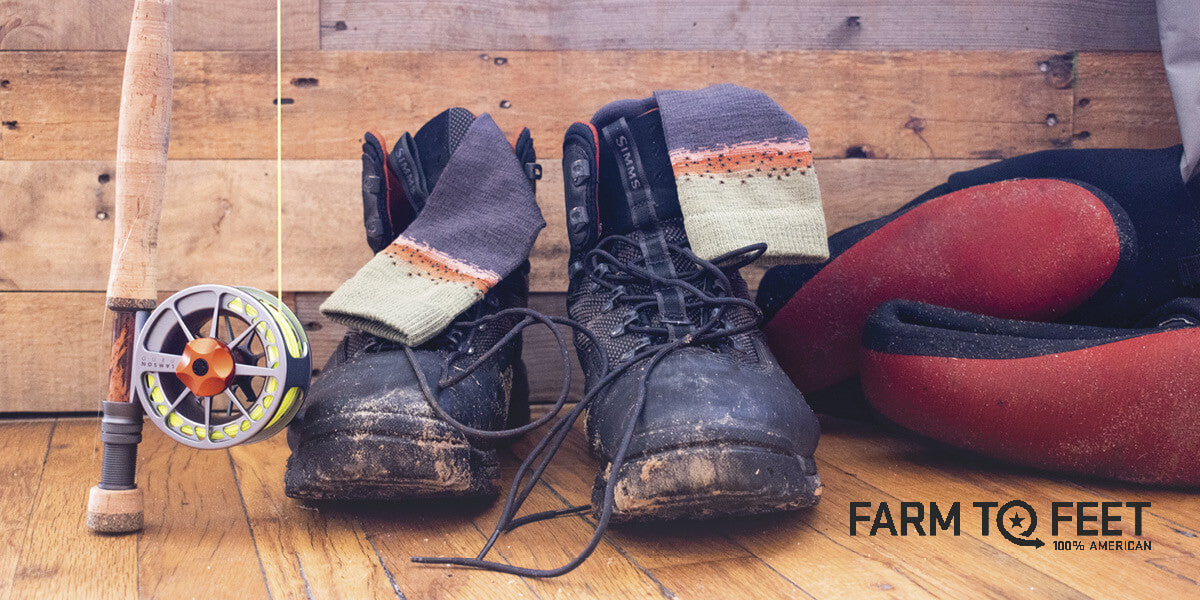 A pair of boots with Farm to Feet socks on a wooden floor, next to a fishing rod.
