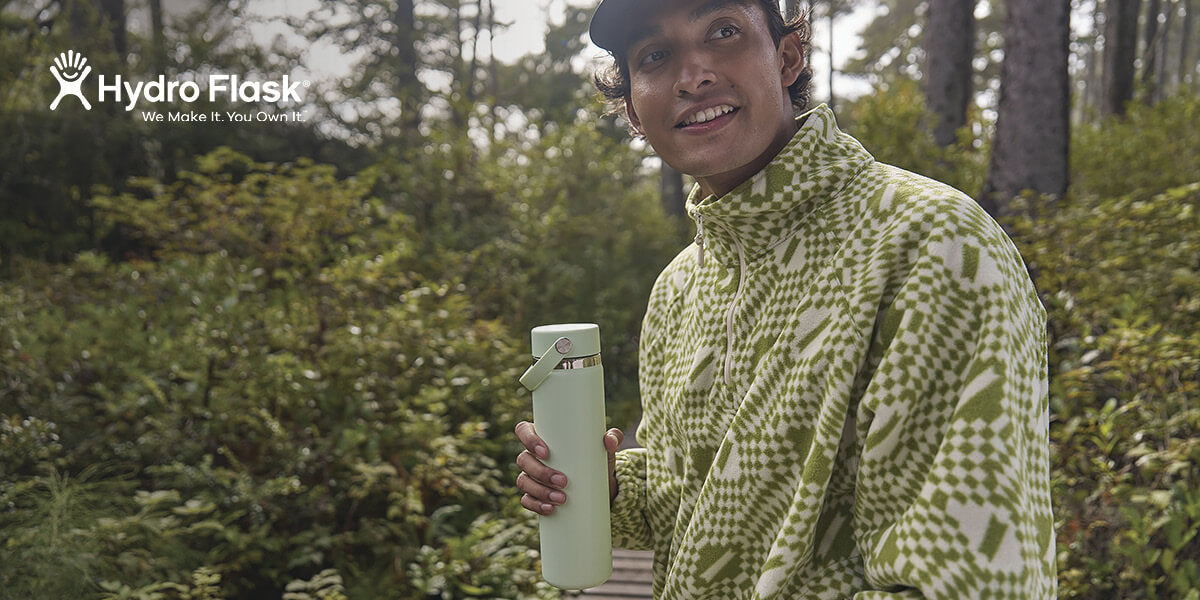 A person holding an Aloe green Hydro Flask water bottle outdoors.