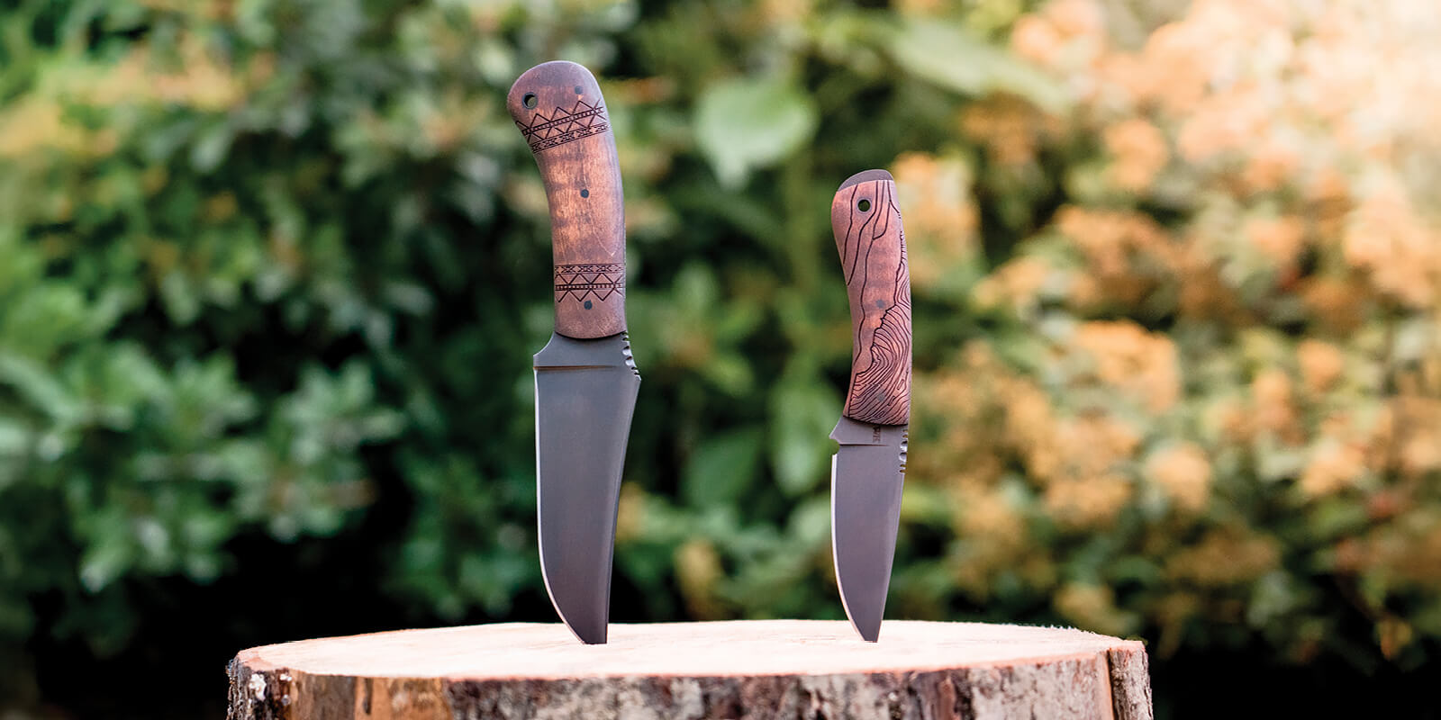 Two Winkler knives with wooden handles displayed on a wooden block against a blurred outdoor background, with the Blue Ridge featuring a sculpted handle on the left and The General, a Mast General Store exclusive on the right