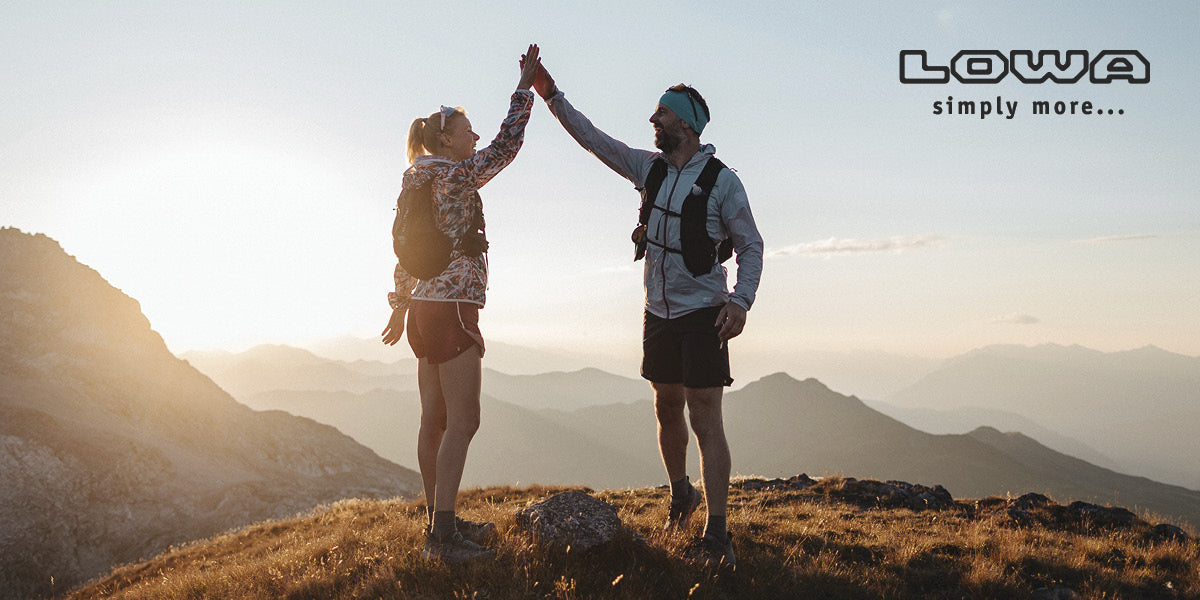 Two people high-fiving on a mountain top wearing LOWA hiking shoes.