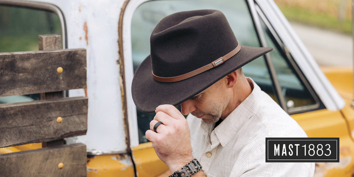 Man wearing a Mast 1883 brown hat in front of an old truck.