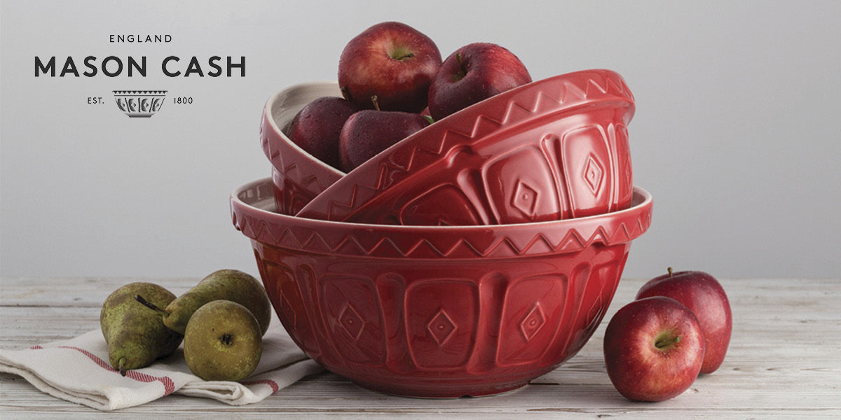 Red Mason Cash mixing bowls with apples and pears on a white wooden surface.