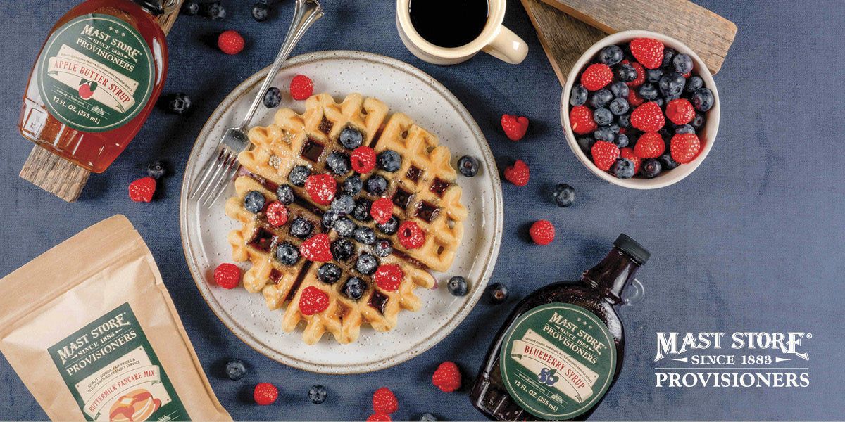 Waffles with berries on a plate, surrounded by Mast Store Provisioners products on a blue surface.