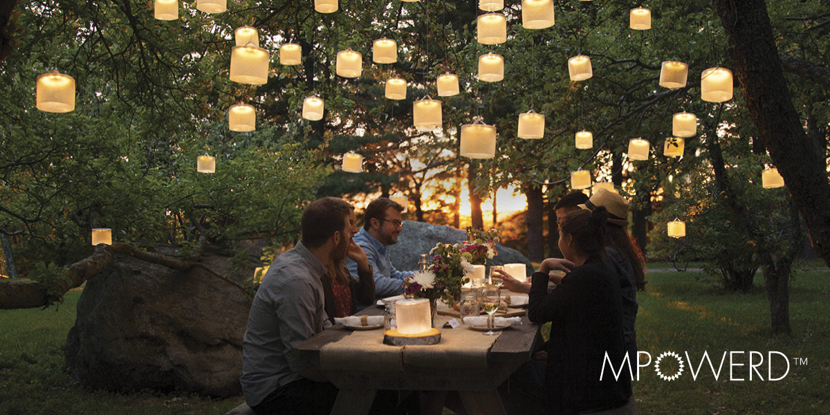 People dining outdoors under MPOWERD floating lanterns in a backyard setting.