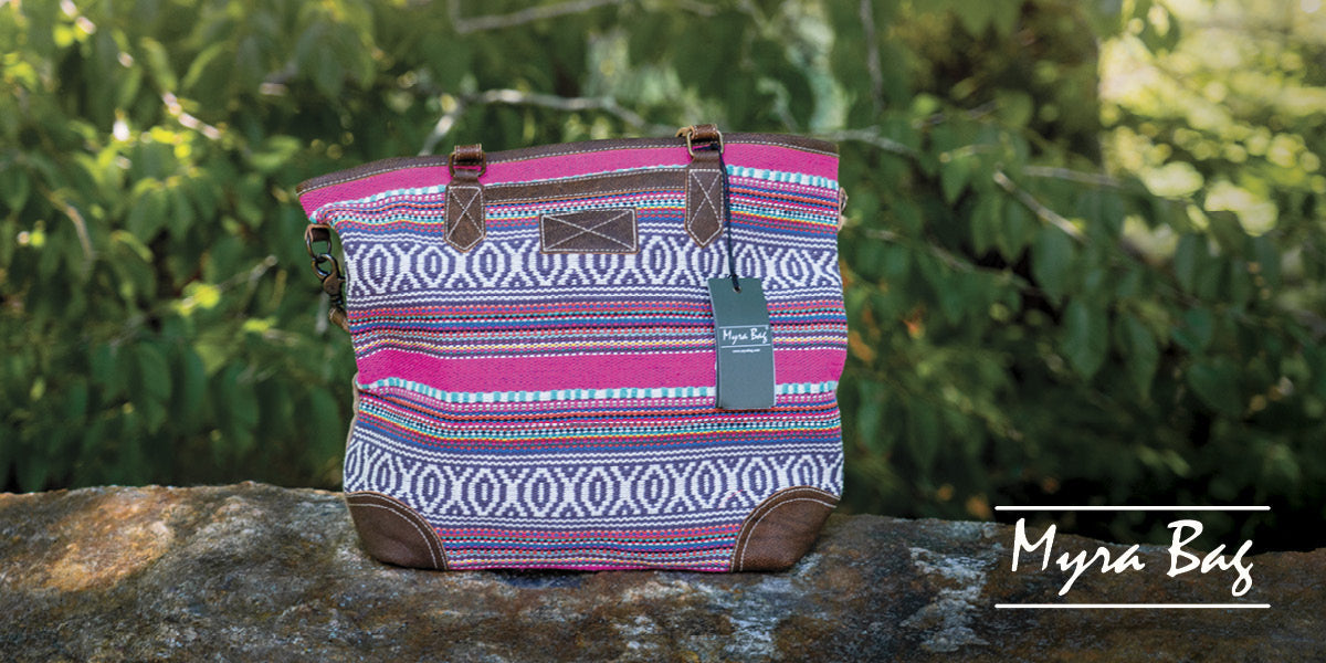 Patterned Myra Bag with brown straps on a stone surface and greenery in the background.