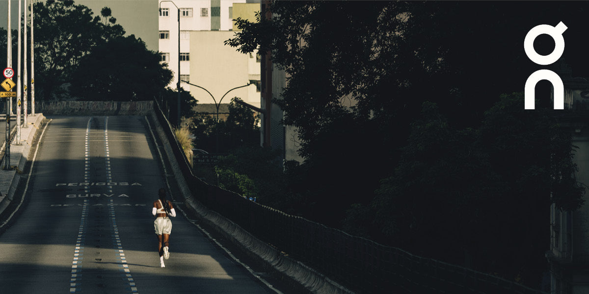 Person wearing On running shoes running on a road with trees and buildings in the background.