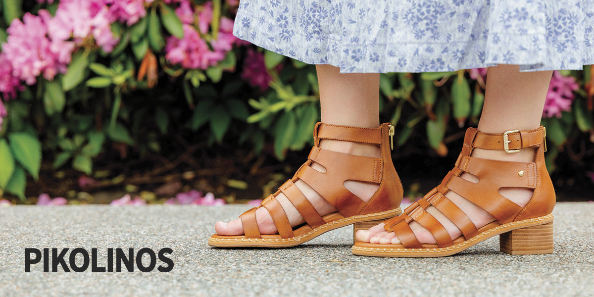 Women wearing Pikolinos brown sandals with a floral dress and pink flowers in the background.