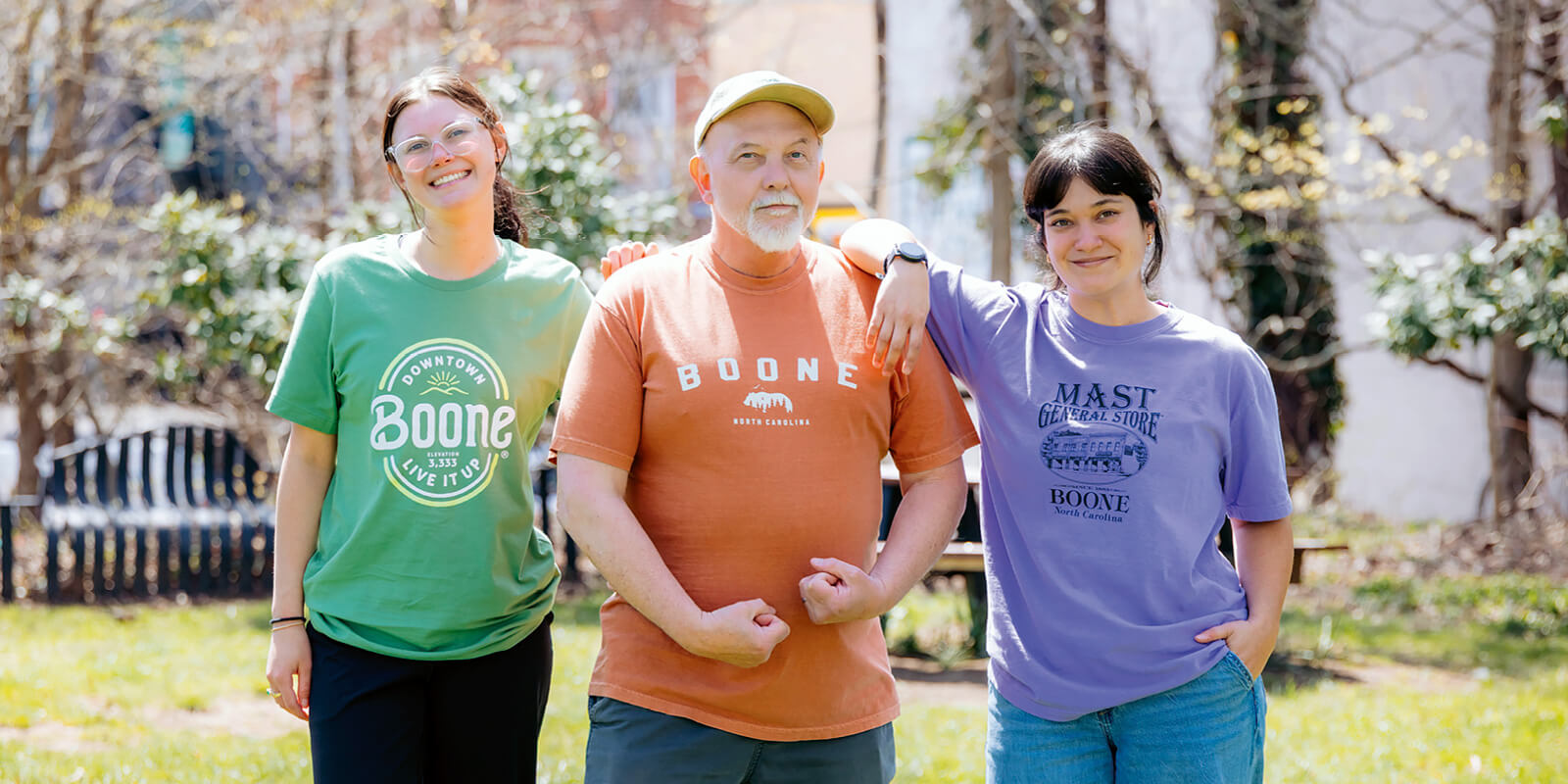 Three people standing together outdoors on a sunny day wearing Boone, North Carolina T‑shirts