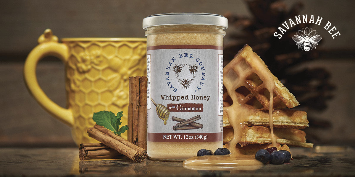 Jar of Savannah Bee Company whipped honey with waffles and cinnamon sticks on a wooden surface.