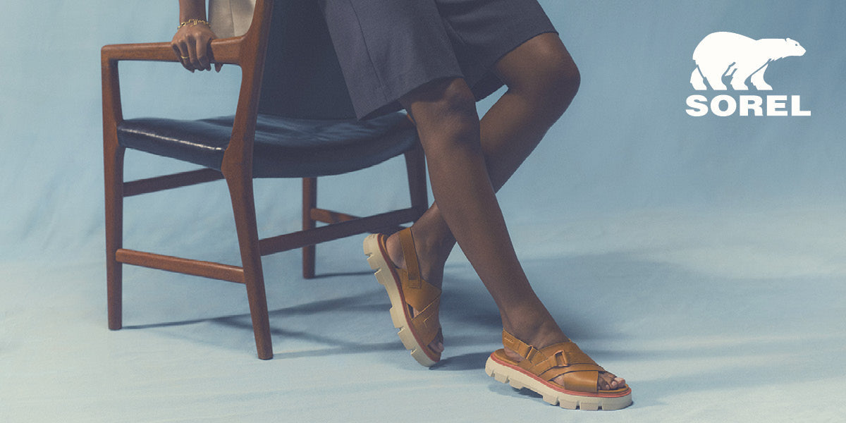 Person wearing brown Sorel shoes sitting on a chair with a blue background