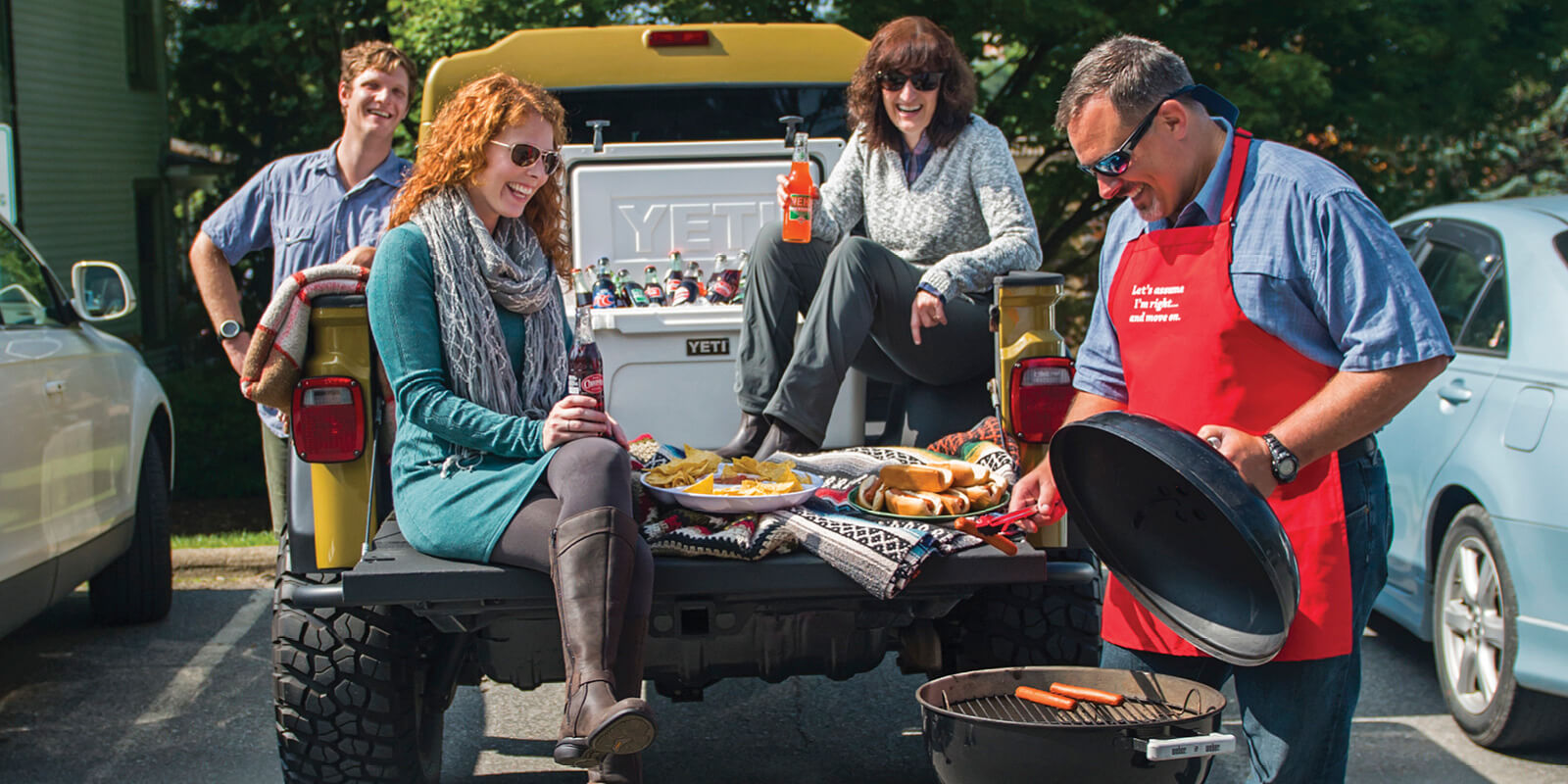 Group of friends tailgating in the back of a Jeep with food and drinks on a sunny afternoon before a game
