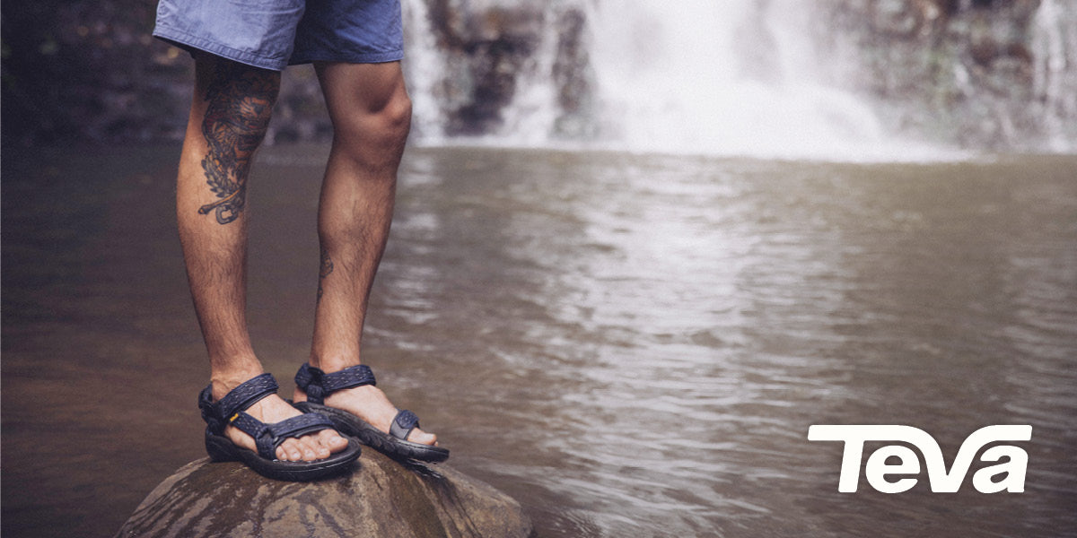 Person wearing Teva sandals standing on a rock with a waterfall in the background