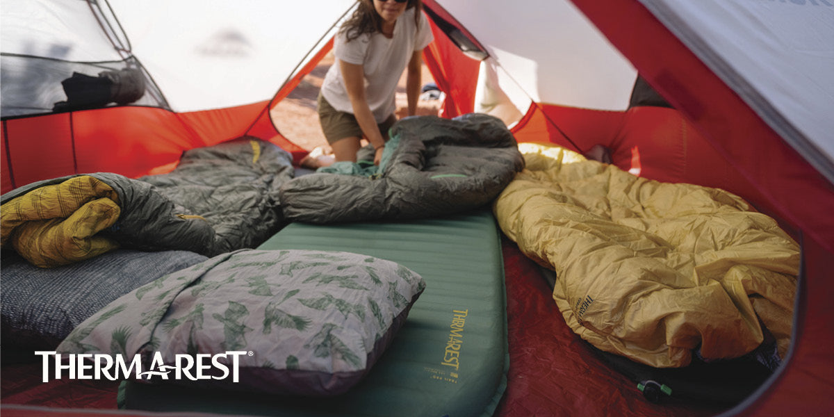 Camping scene with Therm-a-Rest sleeping pads inside a tent, featuring a person setting up the gear.