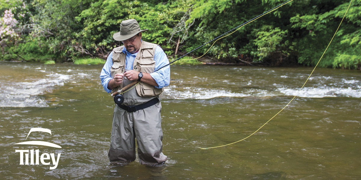 Man fly fishing in a river wearing a Tilley hat.
