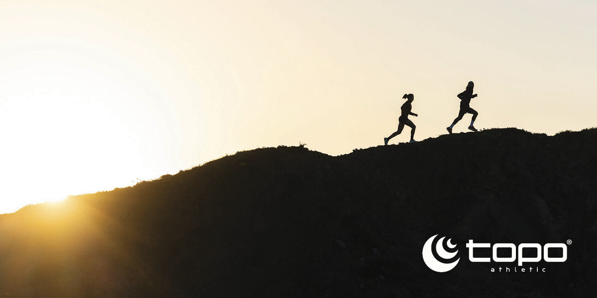 Two people running uphill at sunset while wearing Topo Athletic shoes.