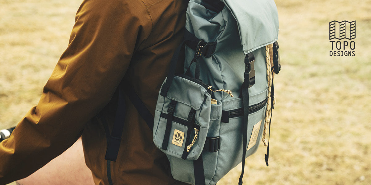 A person riding a bike while wearing a brown long‑sleeve top and a light blue Topo Designs backpack