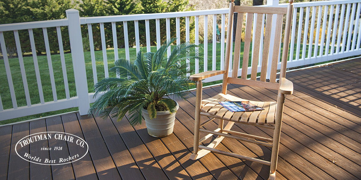 Troutman Chair Co. wooden rocking chair on a wooden deck with a plant and a magazine.