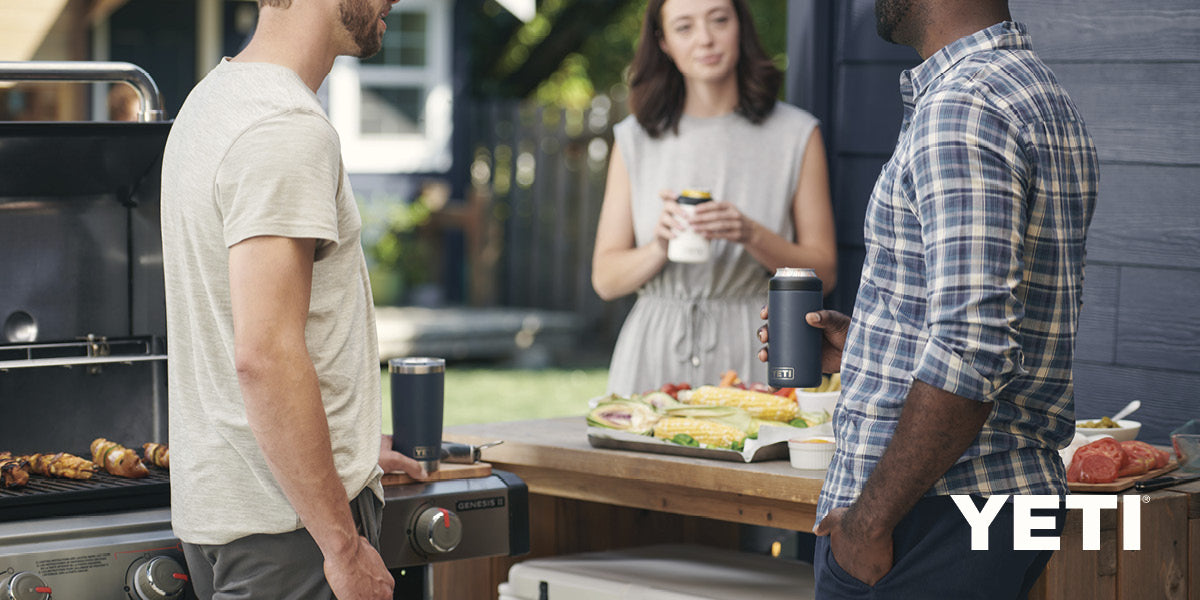 Three people gathered around a grill holding YETI drinkware.