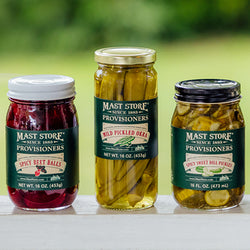 Three jars of Mast Store Provisioner jars of pickles on a white surface with a blurred green background