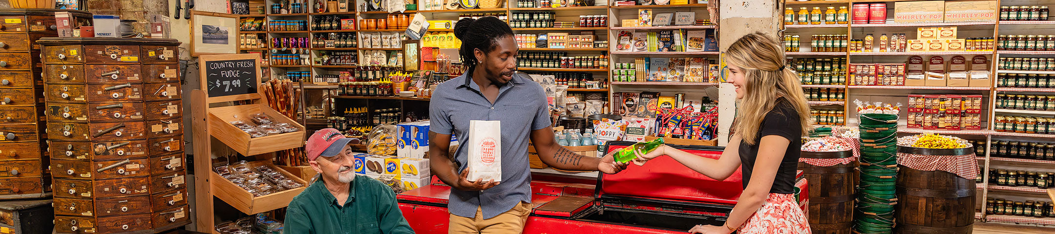 Three people hanging out by the Coca-Cola cooler. A lady is passing a glass bottle of soda to a gentleman holding a bag of popcorn